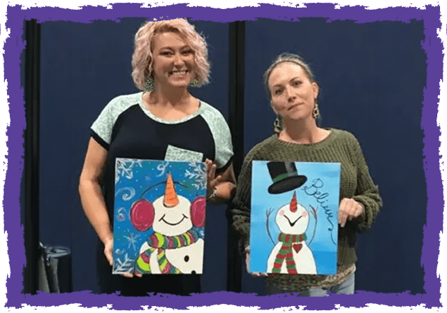 Two women holding up paintings of a snowman.