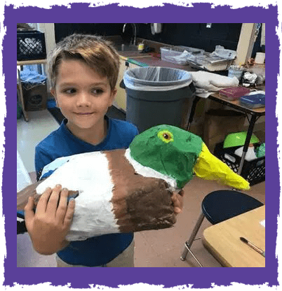 A boy holding a duck made of paper.