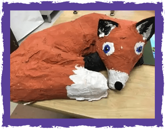 A paper mache fox sitting on top of a table.