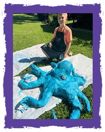 A boy sitting next to an octopus sculpture.