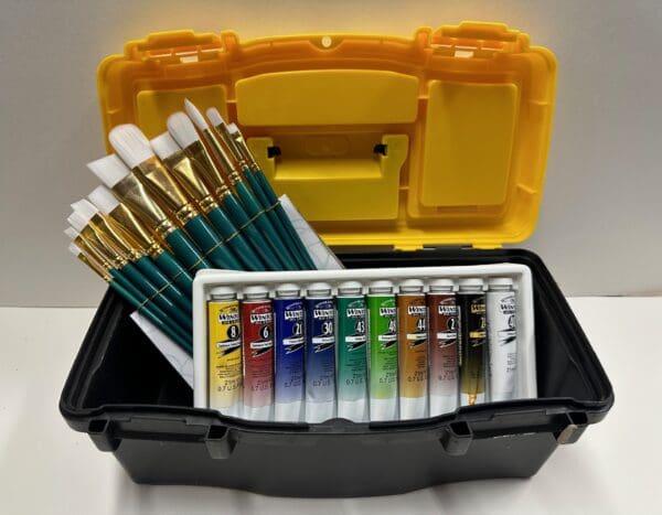 A yellow box with paint brushes and paints in it.