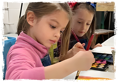 Two young girls are painting with watercolors.