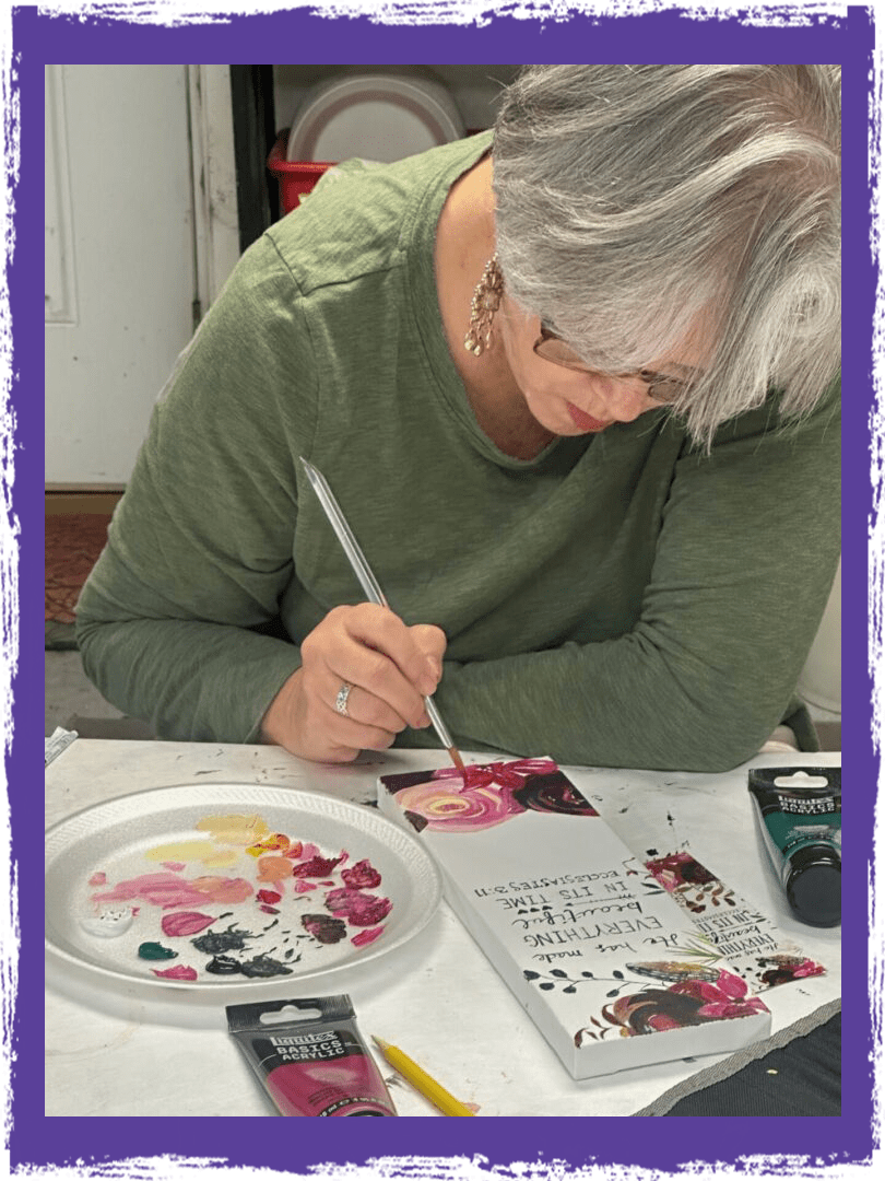 A woman painting with paint brushes on paper.